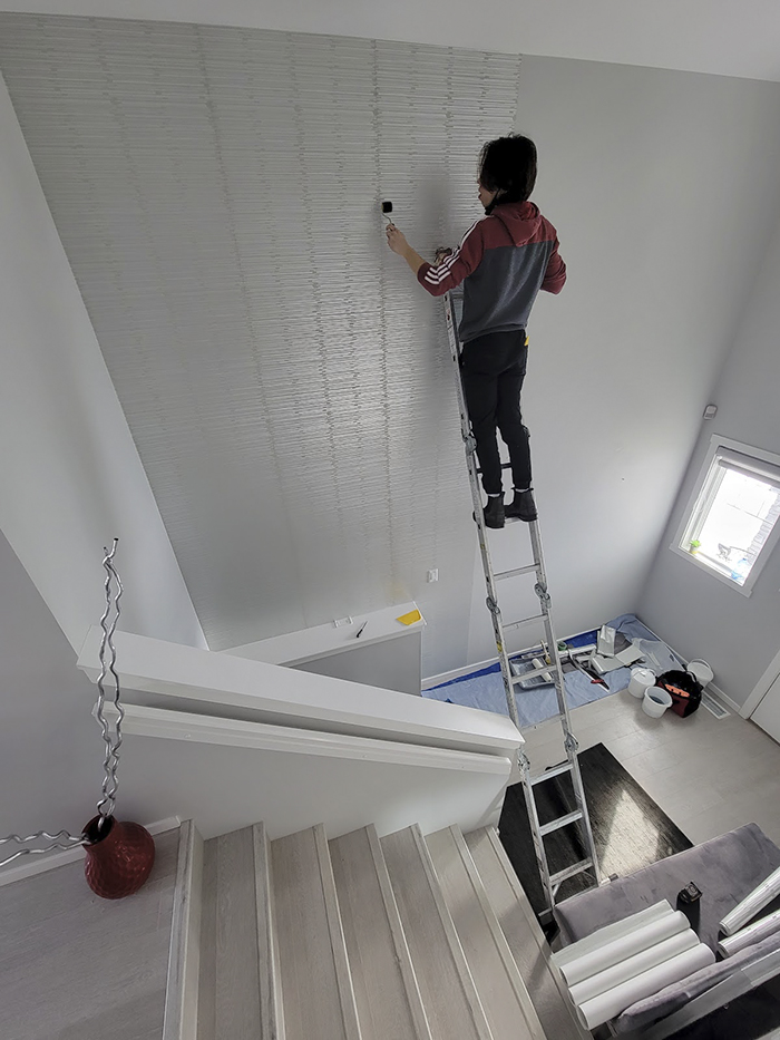 installer standing on ladder and installing silver wallpaper on the wall