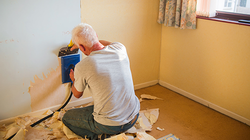 man removing the wallpaper from wall